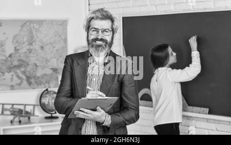 Enseignant vérifiant la bonne réponse. Enseigner avec passion. Matériel pédagogique. Qui est absent aujourd'hui. Petite fille au tableau noir. Retour à l'école. Étudiant et Banque D'Images