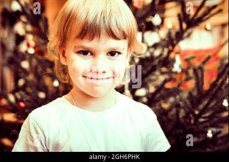 portrait d'un mignon petit heureux candié souriant caucasien petit garçon de cinq ans regarde l'appareil photo contre le fond d'un arbre de noël pendant t Banque D'Images