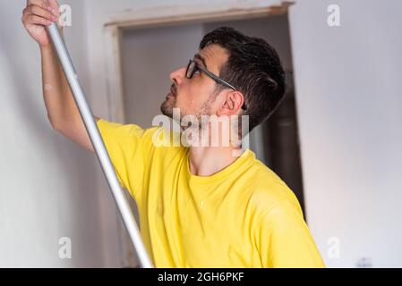 Homme tenant un bâton de rouleau de pinceau tout en peignant le toit d'une maison Banque D'Images