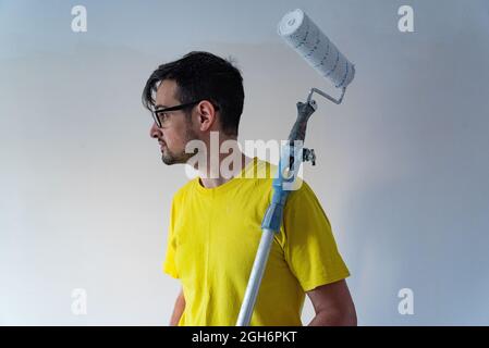 Un homme taché de peinture tenant un rouleau de pinceau monté sur un bâton pour peindre le plafond. Banque D'Images