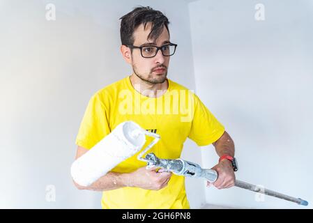 Homme avec un visage surpris tout en tenant le rouleau de pinceau.Gouttes de peinture.Rénovation de la maison Banque D'Images