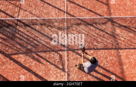 Vue depuis le dessus d'un joueur de paddle-tennis debout près du filet avec la raquette sur un court extérieur.
