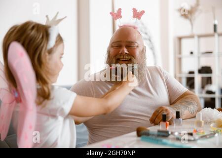 Papa avec serre-tête joue avec la petite fille en costume de fée à la table dans la pièce de lumière Banque D'Images