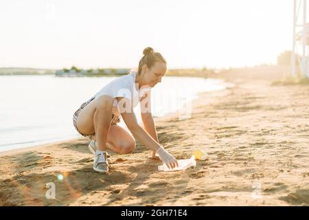 Une jeune femme bénévole satisfaite de ramasser des déchets, des bouteilles en plastique et des tasses à café, nettoyer la plage avec une mer. Femme ramassant des ordures Banque D'Images