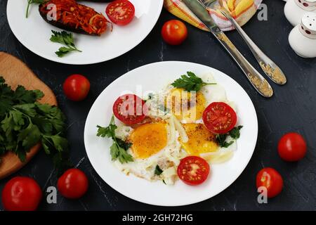 Des œufs brouillés avec des tomates cerises sont situés sur une plaque blanche sur un fond sombre, la photo là des aubergines cuites au four, persil, couverts, vue de dessus Banque D'Images