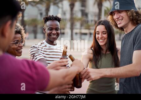 Les jeunes gens interraciaux toaster avec de la bière à l'extérieur. Banque D'Images