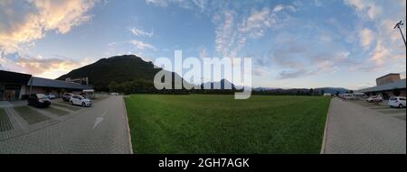 Vue panoramique sur une ville moderne de montagne dans le nord-est de l'Italie, avec le ciel bleu tacheté de nuages et une belle pelouse verte Banque D'Images