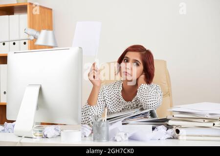 Fatigué désespéré jolie jeune femme d'affaires penchée sur la pile de documents et de lever la main avec le drapeau blanc Banque D'Images