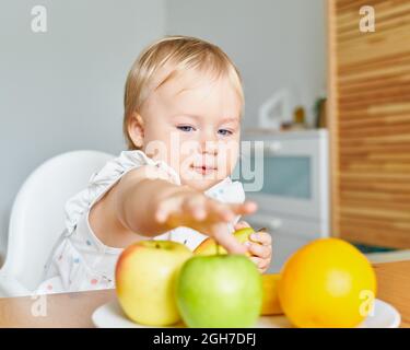 Beau bébé à la recherche de fruits sur l'assiette. Habitudes alimentaires saines. Banque D'Images