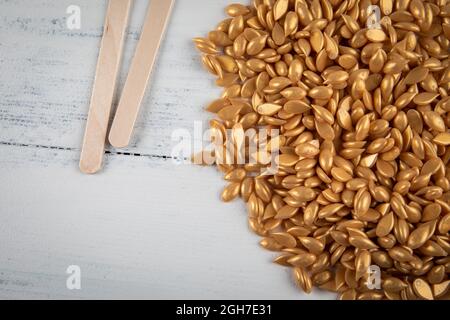 Granules de cire dépilatoire jaune sur une surface en bois blanc. Banque D'Images