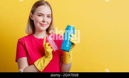 Jeune blonde heureuse femme souriante prête à nettoyer la maison avec des fournitures de ménage isolées sur fond jaune de couleur. Femme Portrait avec nettoyage Banque D'Images
