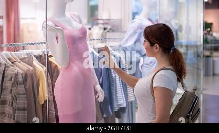 Femme caucasienne regardant une fenêtre de magasin et rêvant d'une robe. Banque D'Images