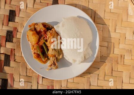 Une assiette contenant de la nourriture de base pap pour farine de maïs africaine traditionnelle et du ragoût de poulet Banque D'Images