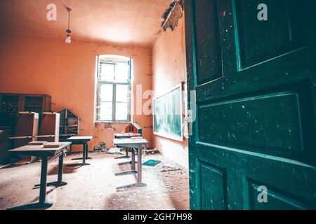 Salle de classe abandonnée avec des bureaux devant un tableau noir d'époque Banque D'Images