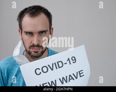 Un homme de nationalité caucasienne avec un masque médical sur le fond d'une notice avec l'inscription: Covid -19 nouvelle vague. Le concept de co Banque D'Images