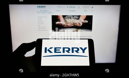 Personne tenant un téléphone portable avec le logo de la compagnie alimentaire irlandaise Kerry Group plc à l'écran en face de la page Web d'affaires. Mise au point sur l'affichage du téléphone. Banque D'Images