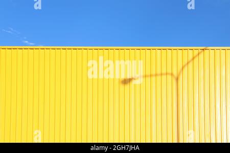 un mur en métal jaune vif reflétant le soleil de l'après-midi avec l'ombre d'un poteau de lumière qui le jette Banque D'Images