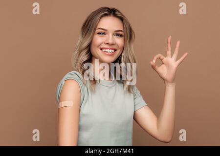 Vaccination Covid-19. Bonne jeune fille montrant le bras avec le plâtre après l'injection du vaccin coronavirus. Banque D'Images