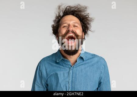 hapy jeune homme en chemise en denim avec une longue barbe s'amusant et riant, hurlant et posant sur fond gris en studio Banque D'Images