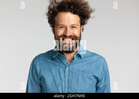 portrait d'un jeune homme heureux avec moustache et barbe portant une chemise en denim, en étant excité et souriant sur fond gris en studio Banque D'Images