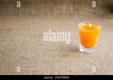 Bougie orange dans un verre avec un fond brun de texture en toile de sackCloth Banque D'Images