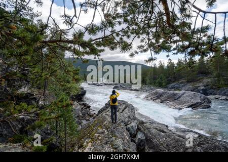 Vue arrière d'une personne portant une veste jaune prenant des photos de la cascade de Pollfoss, rivière Otta, Oppland, Norvège Banque D'Images