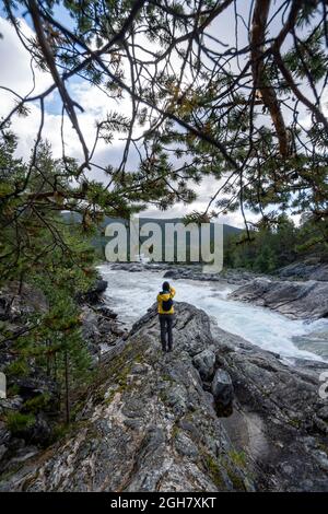 Vue arrière d'une personne portant une veste jaune prenant des photos de la cascade de Pollfoss, rivière Otta, Oppland, Norvège Banque D'Images