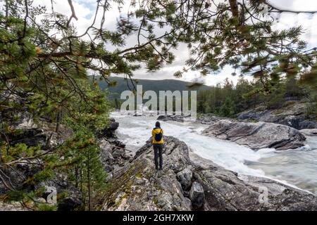 Vue arrière d'une personne portant une veste jaune prenant des photos de la cascade de Pollfoss, rivière Otta, Oppland, Norvège Banque D'Images