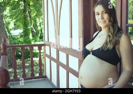 Jeune femme enceinte de sept mois vêtue de bikini noir et de jeans Banque D'Images