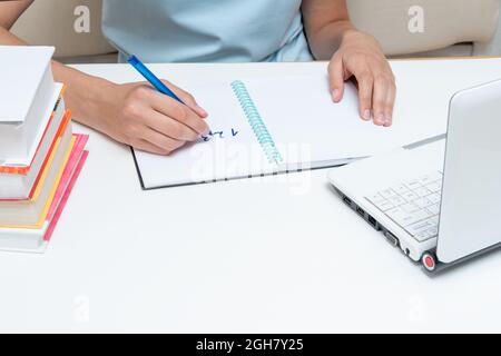 Main d'étudiant tenant un stylo, écrivant dans un bloc-notes l'activité, assis devant un ordinateur portable et des livres. Concept de préparation de l'examen. Retour à sch Banque D'Images