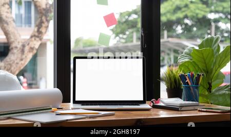 Ordinateur portable avec écran blanc sur bureau en bois, espace de travail technique avec dessin de casque de sécurité. Banque D'Images