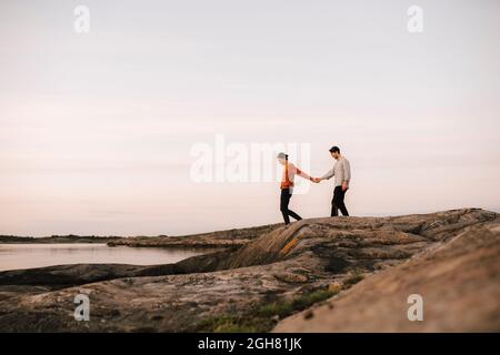 Couple gay tenant les mains tout en marchant sur le bord du lac contre le ciel Banque D'Images