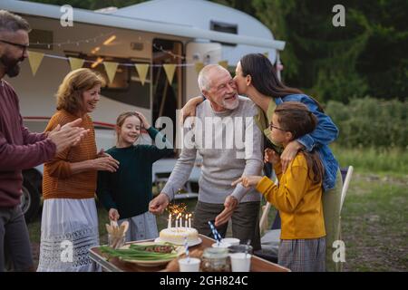 Homme senior célébrant l'anniversaire en plein air au camping, voyage de vacances en caravane familiale de plusieurs générations. Banque D'Images