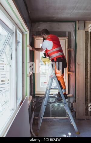 Longueur totale d'un ouvrier de construction se tenant sur une échelle de travail sur le site Banque D'Images