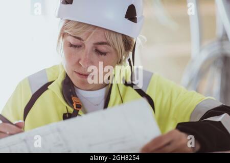 Femme de construction analysant le plan d'étage pendant son travail sur le chantier Banque D'Images