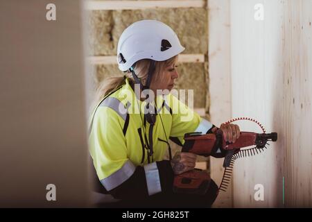 Femme de construction utilisant un outil de travail sur le mur pendant le travail sur le chantier Banque D'Images