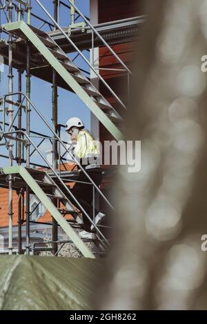 Une entrepreneur de bâtiment pleine longueur parle sur un téléphone intelligent tout en se déplaçant sur des marches sur le chantier de construction Banque D'Images