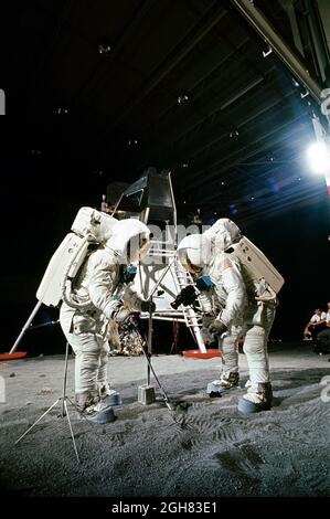 Deux membres de la mission d'atterrissage lunaire Apollo 11 participent à une simulation du déploiement et de l'utilisation d'outils lunaires à la surface de la lune lors d'un exercice d'entraînement au bldg 9, le 22 avril 1969. L'astronaute Edwin E. Aldrin Jr. (À gauche), pilote de module lunaire, utilise une pelle et une pince pour prélever l'échantillon. L'astronaute Neil A. Armstrong, commandant d'Apollo 11, tient le sac pour recevoir l'échantillon. En arrière-plan se trouve une maquette de module Lunar. Les deux hommes portent des unités de mobilité Extravehicular (EMU) Banque D'Images