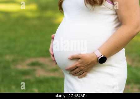 Photo en gros plan sur les mains d'une femme enceinte touchant son ventre à l'extérieur Banque D'Images