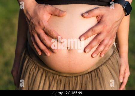 Vue rapprochée des mains d'un homme sur le ventre d'une femme enceinte à l'extérieur Banque D'Images