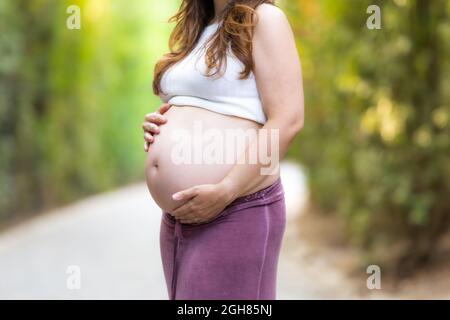 Vue rapprochée des mains d'une femme enceinte adulte dans son ventre à l'extérieur Banque D'Images