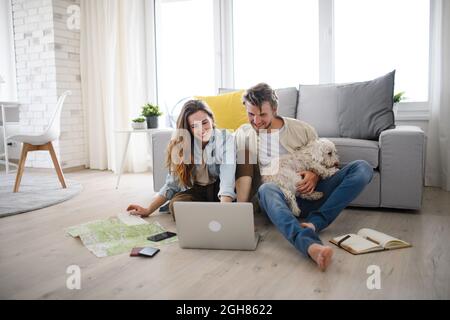 Un jeune couple heureux amoureux de la planification de vacances de chien à l'intérieur à la maison, en utilisant un ordinateur portable. Banque D'Images