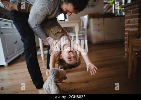 Père mûr avec une petite fille jouant à l'intérieur à la maison, la tenant à l'envers. Banque D'Images