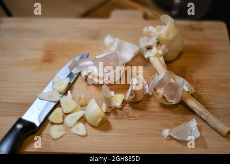 Gousses d'ail fraîchement coupées, allium sativum, car elles ont été extraites de l'ampoule, tranchées sur une planche à pain en bois dans une cuisine domestique Banque D'Images