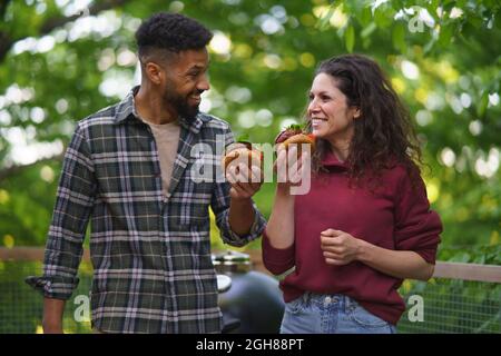 Couple heureux se reposer et manger des hamburgers à l'extérieur dans une maison d'arbre, week-end loin et concept numérique de détox. Banque D'Images