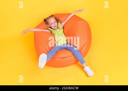 Portrait d'une jeune fille de préadolescence gaie attrayante couché dans un fauteuil de haricot doux reposant isolé sur un fond de couleur jaune vif Banque D'Images