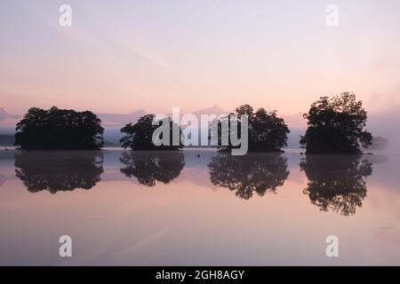 Une rangée de quatre petites îles se reflète dans un lac juste avant le lever du soleil Banque D'Images