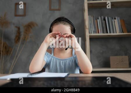 l'enfant est fatigué d'étudier. enseignement à la maison, devoirs. la fille frotte ses yeux de la fatigue, de la lecture de livres et de manuels scolaires. Banque D'Images