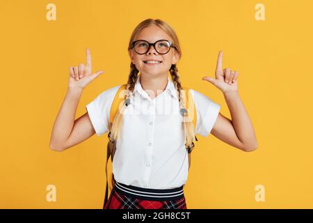 Souriant assez adolescente blanche blonde fille en lunettes montre les pouces jusqu'à l'espace libre Banque D'Images