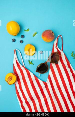 Maillot de bain rayé rouge vif pour femmes, pêches, citrons, lunettes de soleil sur fond bleu vif. Concept de voyage. Flat lay, vue de dessus. Banque D'Images